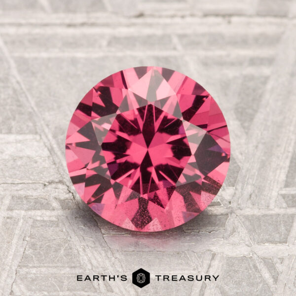 2.02-Carat Mahenge Garnet A 2.02-carat round-cut Mahenge Garnet is displayed on a textured metallic surface with "EARTH'S TREASURY" at the bottom.