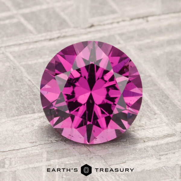 2.00-Carat Mahenge Garnet A round, faceted 2.00-carat Mahenge Garnet gemstone is showcased on a textured surface with the text "EARTH'S TREASURY" at the bottom.