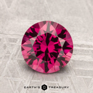 A 1.97-carat Mahenge Garnet, round and faceted, is displayed on a textured surface with "EARTH'S TREASURY" shown below.