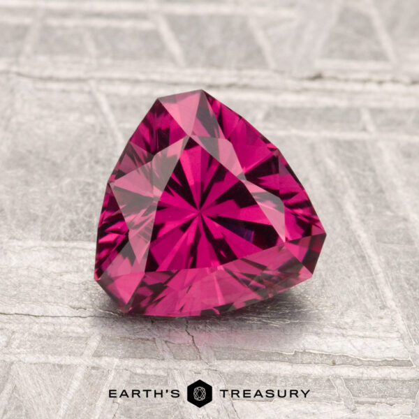 1.62-Carat Mahenge Garnet A vivid, trillion-cut 1.62-carat Mahenge Garnet gemstone displayed on a textured gray surface with the "Earth's Treasury" logo below.