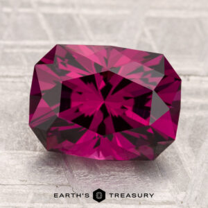 A faceted, deep pink 4.39-carat Umbalite garnet with an octagonal shape is displayed on a light, textured surface. The text "Earth's Treasury" appears at the bottom.