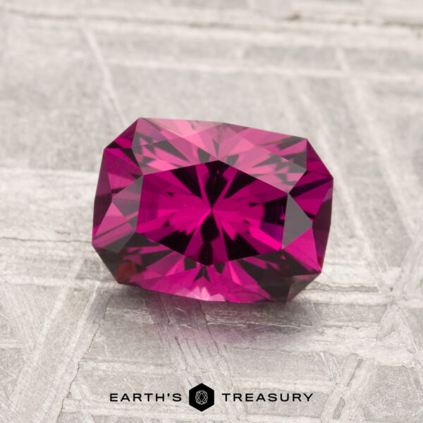 1.79-Carat Umbalite Garnet A 1.79-carat Umbalite garnet with a faceted, deep pink hue rests on a textured light gray surface, with "EARTH'S TREASURY" at the bottom.