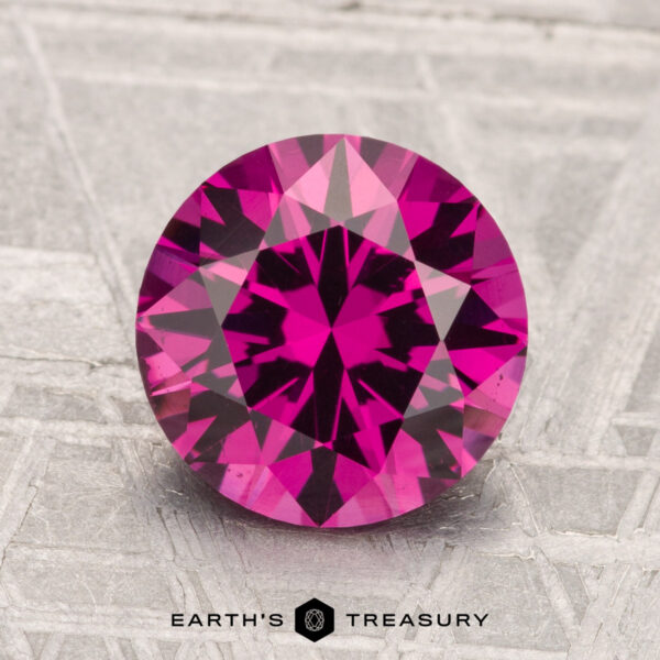 2.56-Carat Umbalite Garnet A 2.56-carat faceted Umbalite Garnet in deep pink is displayed on a textured gray surface with "Earth's Treasury" text below.