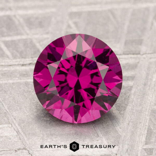 2.20-Carat Umbalite Garnet A 2.20-carat round, faceted deep pink Umbalite Garnet is displayed on a textured light gray surface with the text "Earth's Treasury" below.