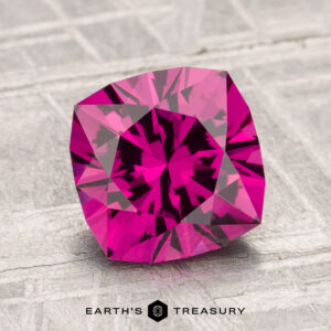 A vibrant, faceted 2.53-carat Umbalite Garnet gemstone is displayed on a textured surface with the text "EARTH'S TREASURY" at the bottom.