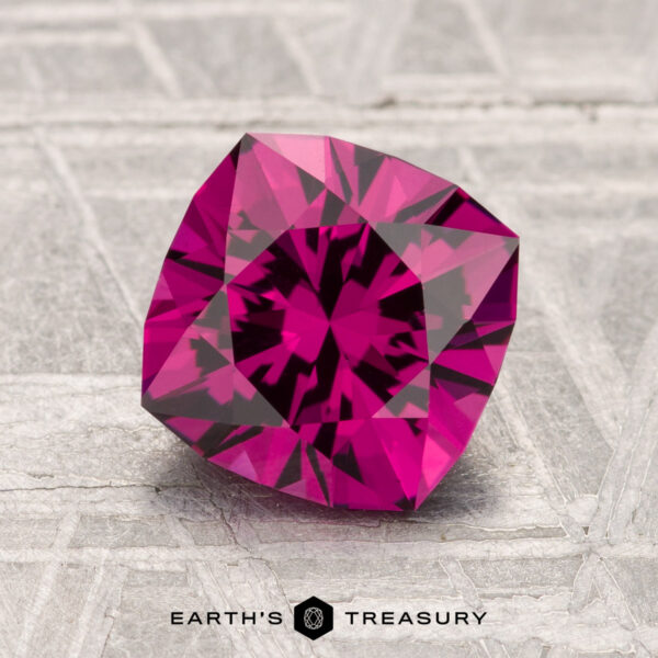 1.95-Carat Umbalite Garnet A 1.95-carat cushion-cut Umbalite Garnet with intricate facets rests on a textured gray surface, with "Earth's Treasury" displayed below.