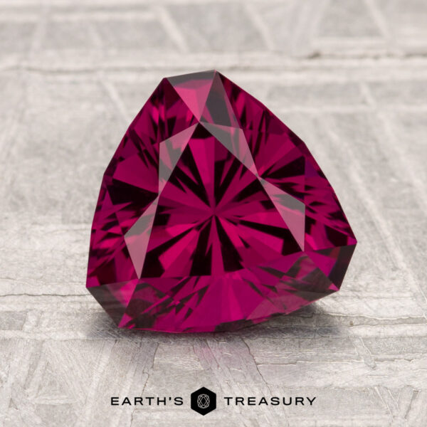 2.64-Carat Umbalite Garnet A 2.64-carat Umbalite Garnet in a deep pink trillion cut rests on a textured, light surface with "Earth's Treasury" beneath it.