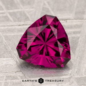 A vivid, trilliant-cut 2.55-carat Umbalite Garnet rests on a textured gray surface with the "Earth's Treasury" logo beneath it.
