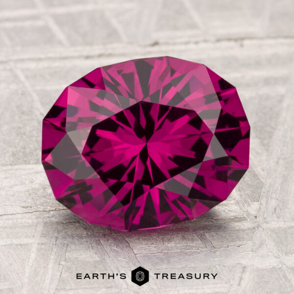 3.62-Carat Umbalite Garnet A 3.62-carat Umbalite Garnet, featuring a deep pink hue and faceted cut, is displayed on a textured surface with the "Earth’s Treasury" logo at the bottom of the image.