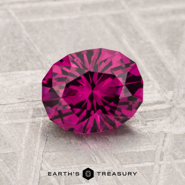 1.61-Carat Umbalite Garnet A 1.61-carat Umbalite garnet with a round cut and intricate facets is displayed on a textured gray surface near the Earth’s Treasury logo.