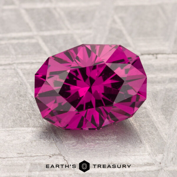 2.45-Carat Umbalite Garnet A 2.45-carat, oval faceted Umbalite Garnet gemstone rests on a metallic textured surface with the "Earth's Treasury" logo at the bottom.