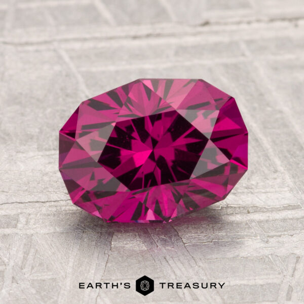 2.38-Carat Umbalite Garnet A 2.38-carat Umbalite Garnet, faceted in deep pink, is displayed on a textured light gray surface with the "Earth's Treasury" logo at the bottom.
