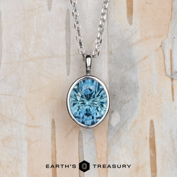 The "Foggy" pendant in 14k white gold with 1.37-carat Montana sapphire The "Foggy" pendant in 14k white gold features a 1.37-carat oval Montana sapphire on a chain, shown against a light, textured background. "EARTH'S TREASURY" logo and text are at the bottom.