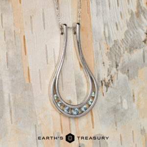 The "Twilight" ring keeper necklace in 14K white gold features a teardrop design with seven small gemstones at the base, shown on a light wooden background with the "Earth's Treasury" logo below.