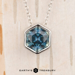 The Build Your Own "Shimmer" pendant in 14k white gold features a 1.62-carat Montana sapphire, shown against a light textured background with the "Earth's Treasury" logo at the bottom.