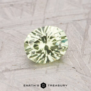 A round, faceted 0.92-carat Grossular Garnet gemstone rests on a textured gray surface with the "Earth's Treasury" logo at the bottom.