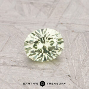 A 0.68-carat round, faceted Light Mint Green Grossular Garnet rests on a textured gray surface with the "Earth's Treasury" logo at the bottom.