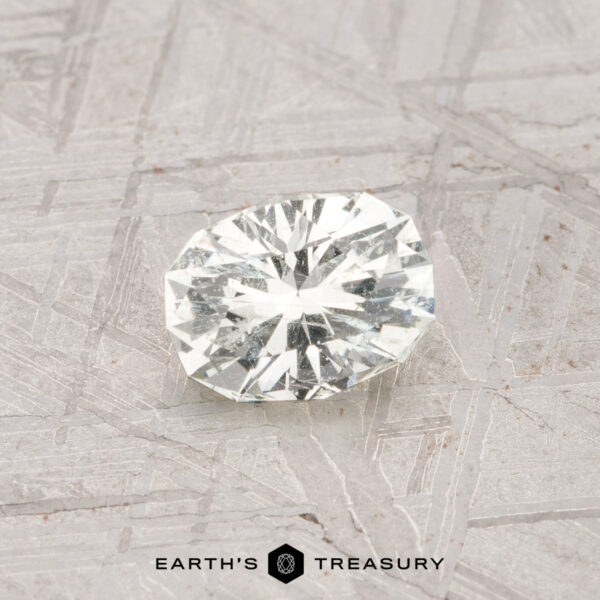 0.62-Carat Grossular Garnet A faceted 0.62-carat Grossular Garnet rests on a textured, light-colored surface featuring the "EARTH'S TREASURY" text and logo at the bottom.