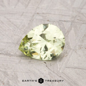 A 0.98-carat pale mint green Grossular Garnet gemstone, pear-shaped, is displayed on a textured gray background. "EARTH'S TREASURY" appears at the bottom of the image.