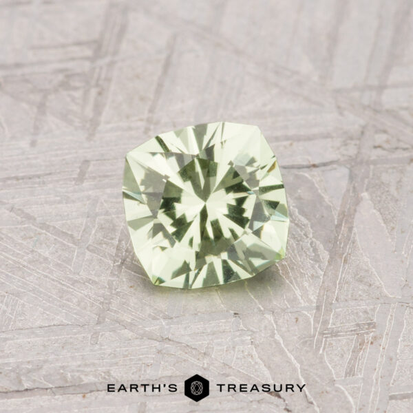 0.59-Carat Grossular Garnet A 0.59-Carat Grossular Garnet with a cushion cut and pale mint green hue is shown on a textured gray surface, featuring the "EARTH'S TREASURY" logo and text at the bottom.