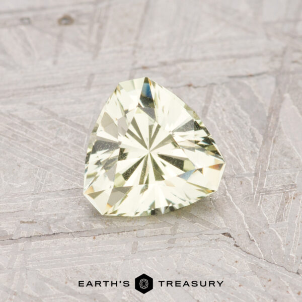 0.83-Carat Grossular Garnet A pale mint green, trillion-cut grossular garnet weighing 0.83 carats rests on a textured light gray surface with the text "Earth's Treasury" at the bottom.