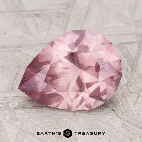 3.12-Carat Garnet A 3.12-carat pink, pear-shaped faceted garnet rests on a textured surface with "Earth's Treasury" at the bottom.