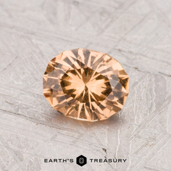 0.97-Carat Grossular Garnet A 0.97-carat round, faceted Grossular Garnet with a peach hue is displayed on a gray, patterned surface. "EARTH'S TREASURY" logo and text are visible at the bottom of the image.