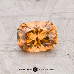 A 1.40-carat rectangular, faceted orange grossular garnet is displayed on a light, textured surface with "Earth's Treasury" written below.