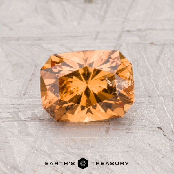 1.40-Carat Grossular Garnet A 1.40-carat rectangular, faceted orange grossular garnet is displayed on a light, textured surface with "Earth's Treasury" written below.