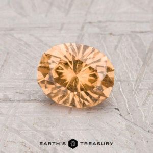 A 1.04-carat, faceted oval Grossular garnet gemstone with a yellow hue is displayed on a textured gray surface, featuring the "Earth's Treasury" branding at the bottom.