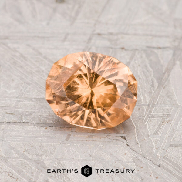 1.09-Carat Grossular Garnet A 1.09-carat oval-cut Grossular Garnet gemstone is showcased on a gray, patterned surface with "Earth's Treasury" displayed at the bottom.