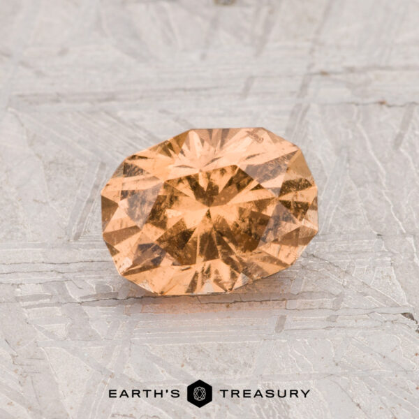 1.17-Carat Grossular Garnet A 1.17-carat grossular garnet, oval and faceted with an orange hue, rests on a textured metallic surface displaying "EARTH'S TREASURY" at the bottom.