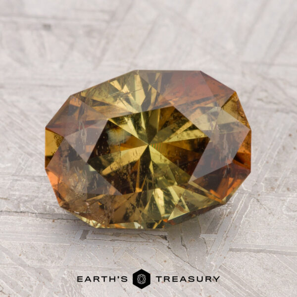 3.42-Carat Andalusite A 3.42-carat, faceted oval Andalusite with yellow and brown hues rests on a textured gray surface. The "EARTH'S TREASURY" logo appears at the bottom.