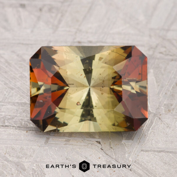 2.52-Carat Andalusite A 2.52-carat Andalusite with rectangular facets and yellow-green and reddish-brown color zones, displayed on a textured gray surface with "Earth's Treasury" below.