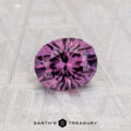 A 0.97-carat color change garnet, round and faceted, is displayed on a textured light surface with "EARTH'S TREASURY" at the bottom.