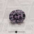 A 0.97-carat color change garnet, round and faceted with a rich purple hue, is shown on a textured surface with "Earth's Treasury" displayed below the gemstone.