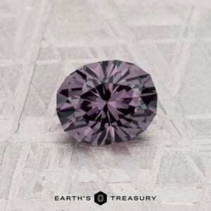A 0.97-carat color change garnet, round and faceted with a rich purple hue, is shown on a textured surface with "Earth's Treasury" displayed below the gemstone.