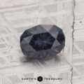 A 1.42-carat color change garnet rests on a textured metallic surface, with "EARTH'S TREASURY" displayed at the bottom.