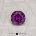 A round, faceted 0.56-carat Color Change Garnet gemstone displayed on a light textured surface with the logo and text "EARTH'S TREASURY" at the bottom.