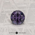 A 0.56-carat color change garnet, round-cut and deep purple, shown on a textured gray surface with "EARTH'S TREASURY" below.