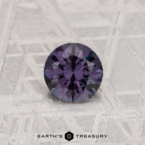 A 0.56-carat color change garnet, round-cut and deep purple, shown on a textured gray surface with "EARTH'S TREASURY" below.