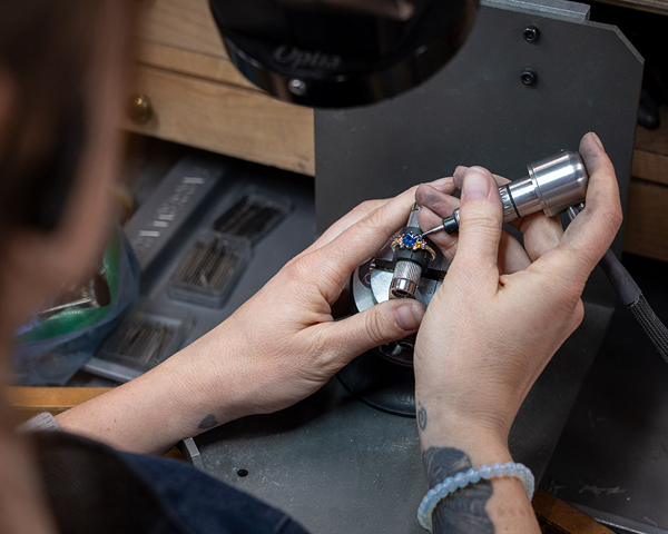 Someone uses the bring-your-design-to-life rotary tool to engrave a ring secured in a vise, adding detailed designs at their workbench.