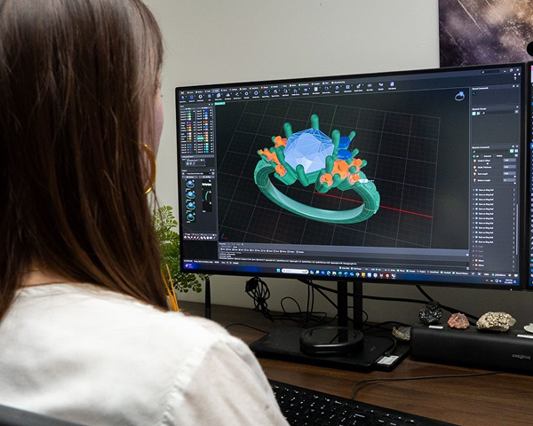 A person uses the connect-with-designer service at their desk to create a digital model of a gemstone ring with 3D design software.