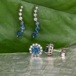 Stacked from 46 images. Method=B (R=9,S=5): A pair of dangling earrings with white and blue stones and round blue stud earrings with a halo of white stones, displayed on a green leaf background.