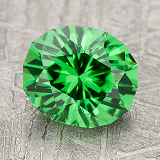 The gem-color-green is an oval-shaped, faceted green gemstone shown on a gray textured surface.