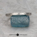 The ET Stock silver textured Straight Astrea Band is displayed on a rough blue gemstone atop a gray patterned surface, with the Earth’s Treasury logo beneath.