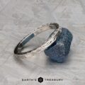 A silver ET Stock band with engraved patterns rests on a rough blue stone against a textured gray background. The text "EARTH'S TREASURY" appears below.