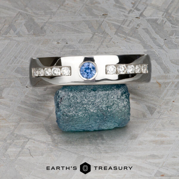 The "Sinai" ring in platinum with medium blue sapphire A ring from "Stacked from 53 images. Method=B (R=9,S=4)" with a central blue gemstone and side stones is balanced on a rough blue crystal, shown above the text "Earth's Treasury.