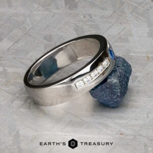 The "Stacked from 54 images. Method=B (R=9,S=4)" ring, featuring five diamonds and a central blue gemstone, is showcased resting on a rough blue mineral atop a textured gray surface.