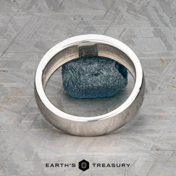 The "Sinai" ring in platinum with medium blue sapphire A "Stacked from 56 images. Method=B (R=9,S=4)" ring is displayed upright around a rough blue stone on a textured metallic surface, with the text "Earth's Treasury" at the bottom—a nod to elegance inspired by Matterhorn’s timeless allure.